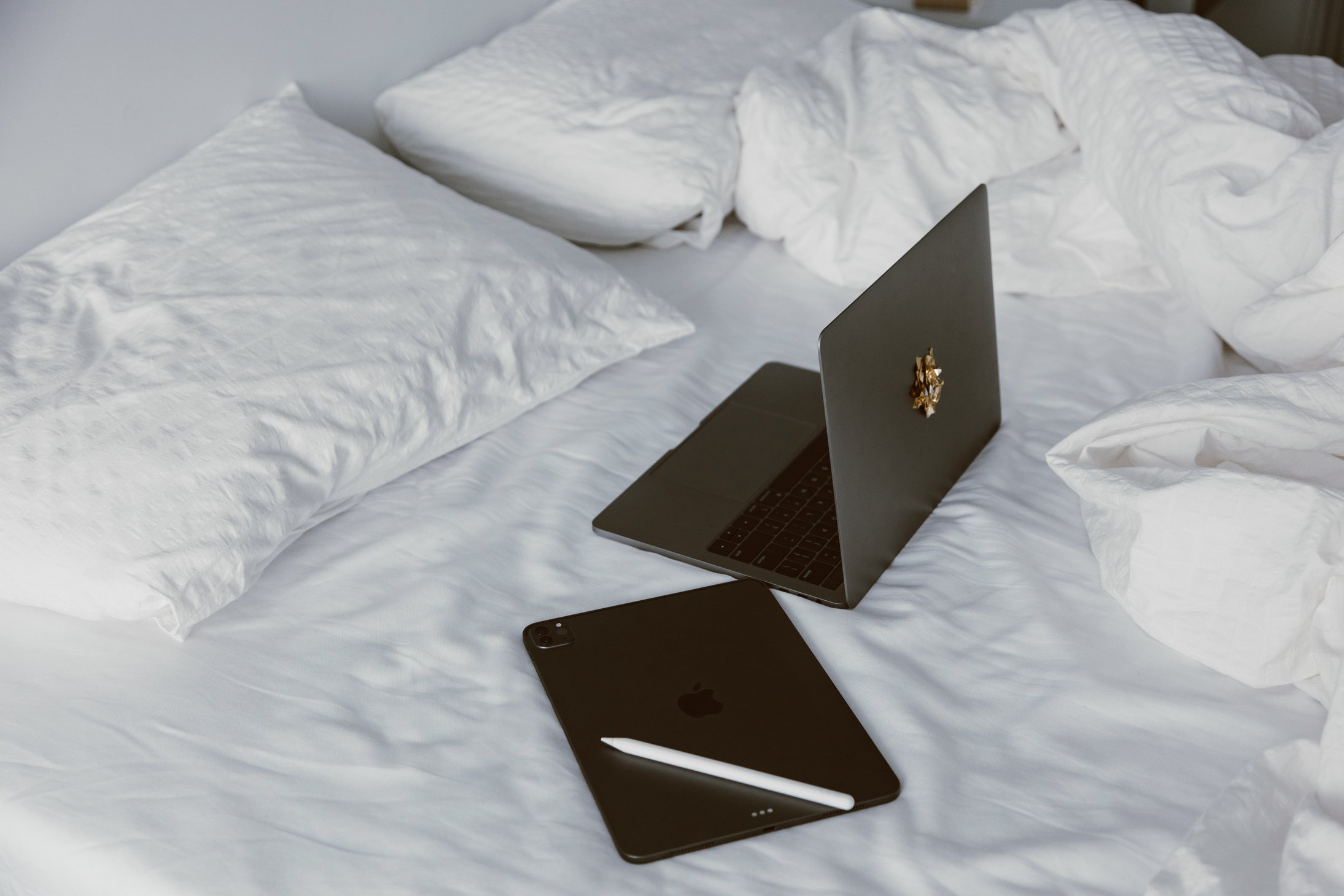 A Black Laptop beside an Ipad on the Bed